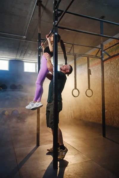 Personal trainer helpt knappe Sportvrouw doen pull up oefening in de sportschool. — Stockfoto