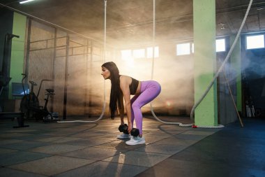 Spor salonunda dumbbells ile egzersiz yapan genç fit kadın.