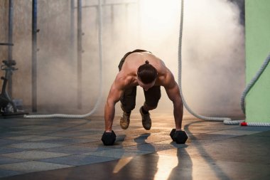 Spor salonunda eğitim sırasında dumbbells ile şınav yapıyor Genç güçlü adam.