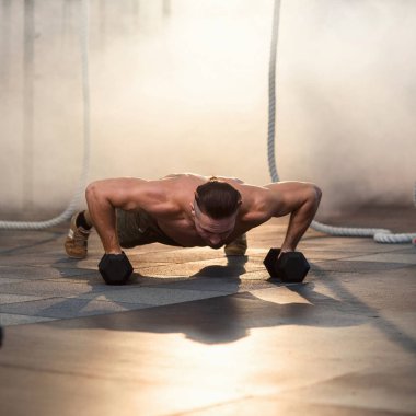 Spor salonunda eğitim sırasında dumbbells ile şınav yapıyor Genç güçlü adam.