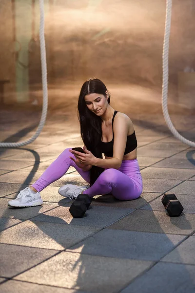 Young sport woman using smartphone during resting after hard training in the gym.