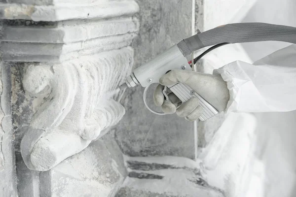 Hand of worker with the gun for serving a high-pressure sand jet. Professional restoration of historical buildind with stone carved decorative elements. — Stock Photo, Image