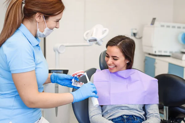 フレンドリーな歯科医は、適切に電気ブラシで彼の歯を磨く方法を患者に示しています。歯のケアと衛生の概念. — ストック写真