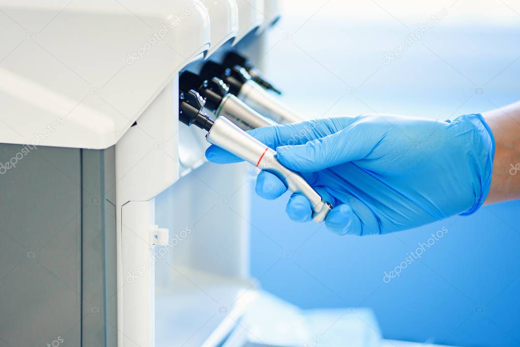 Assistants hand in rubber mitt configures dental equipment in dentists office. Selective focus. Dentistry and teeth care concept.