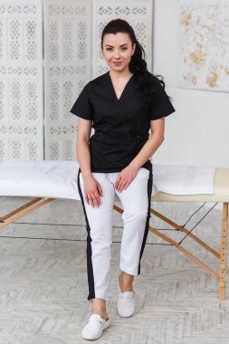 Kameraya bakarak ve modern tıbbi ofis masaj masa arkasında, Doktor gülümseyerek. Sağlık ve tıp kavramı.