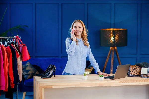 Dizüstü bilgisayar kullanırken akıllı telefonda konuşan genç mutlu kadın blogger.