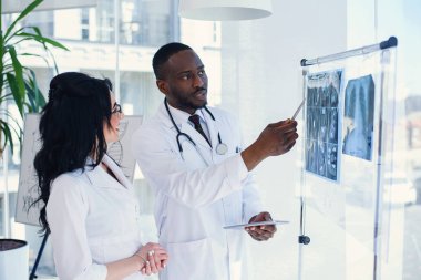 Afrika erkek ve beyaz kadın doktorlar hastanede hastanın MRG sonuçlarını tartışıyor. Beyaz paltolarda stooscopes ile erkek ve kadın doktorlar. Tıbbi ve sağlık konsepti.