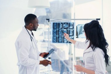Two doctors look at an x-ray and discuss the problem. Medical technicians pointing at MRI x-ray of patient. Radiologist checking x-ray. Medical and radiology concept. clipart