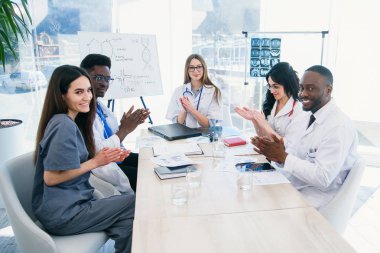 Profesyonel genç doktorlar uluslararası grup ellerini çırparak ve modern bir klinikte bir tıp konferansında gülümseyerek vardır. Tıp ve sağlık kavramı.