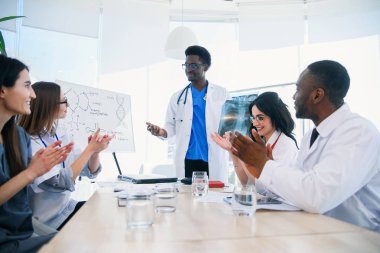 Profesyonel genç doktorlar uluslararası grup ellerini çırparak ve modern bir klinikte bir tıp konferansında gülümseyerek vardır. Tıp ve sağlık kavramı.