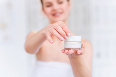 Çekici esmer kadın krem ile kavanoz açılış ve beyaz şık banyoda kameraya gülümseyerek. Portre çekimi.