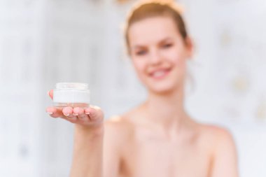 Çekici esmer kadın krem ile kavanoz açılış ve beyaz şık banyoda kameraya gülümseyerek. Portre çekimi.