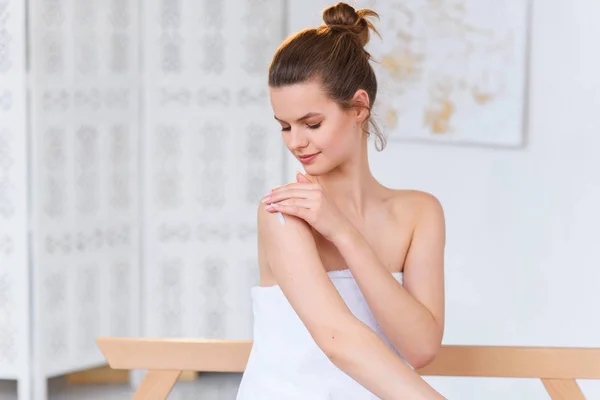 Mulher branca bonito em toalha branca aplicando creme em sua pele antes do procedimento de spa no fundo do salão de beleza branco . — Fotografia de Stock