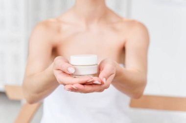 Genç beyaz bir kadının elinde doğal krem ile cam kavanoz. Güzellik, vücut bakımı, cilt bakımı konsepti. Seçici odaklama.