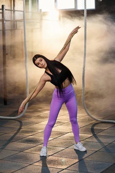 Una hermosa mujer hace ejercicios de calentamiento con barra en el moderno gimnasio con estilo . — Foto de Stock