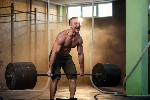 Sportlicher junger Mann hockt mit Langhantel in der Turnhalle. — Stockfoto