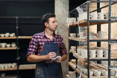 Not defterinde bir şey belirten orta yaş çömlekçi.