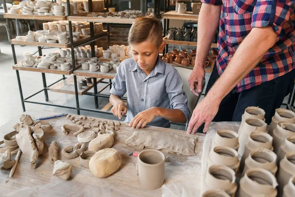 Běloch ve středním věku, který učí malému synovi, jak pracovat s hlinkou na hrnkovém kotouči. — Stock fotografie