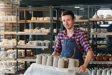 Beyaz erkek çömlekçi çömlek seramik kapları ile tepsi tutan.