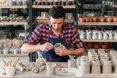 Bir iş üniforması orta yaşlı bir adam büyük bir yaratıcı çömlek atölyesinde fincan kil şeklinde yapmak.
