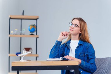 Genç kız beyaz oturma odasında okurken tatil hakkında rüyalar. Dünya ile coğrafya eğitimi. Denim giysiler içinde Sevimli kız öğrenci ev ödevi yapar.