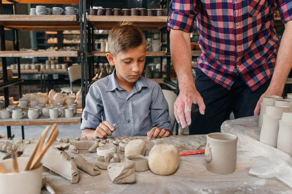 Middle aged caucasian man teaches his little brother to work with clay on pottery workshop. Art work concept.