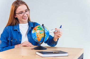 Young beautiful woman moving model of air plane around the globe and dreaming about future vacation abroad. clipart
