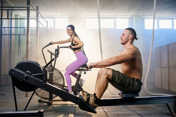 Joven pareja deportiva haciendo ejercicios en los simuladores en el gimnasio . — Foto de Stock