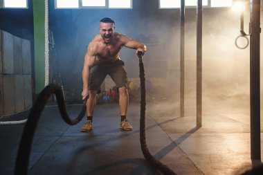 Yakışıklı güçlü adam fitness salonunda savaş halatları ile kaslar için egzersizyapıyor.