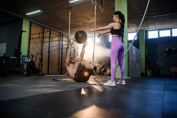 Caucásico hombre deportivo haciendo ejercicio de pelota abdominal con entrenador femenino personal en el gimnasio . — Foto de Stock