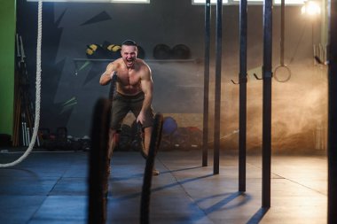 Genç spor adam fitness salonunda savaş halatları ile egzersizleri yapıyor.