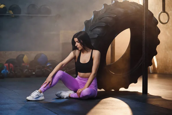 疲惫的运动妇女休息后，训练，而坐在地板上附近的车轮轮胎在健身房. — 图库照片