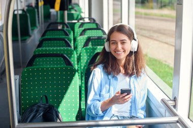 Güzel kadın modern şehir tramvay hareket ederken kulaklık, akıllı telefon ve kahve fincan ile oturur. toplu taşıma da gezi zevk.
