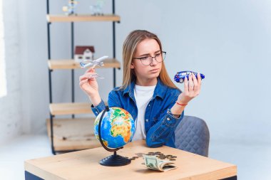 Genç kadın bir uçak ve araba modeli tutuyor ve seyahat için daha iyi bir araç seçiyor. Seyahat ve tatil kavramı.