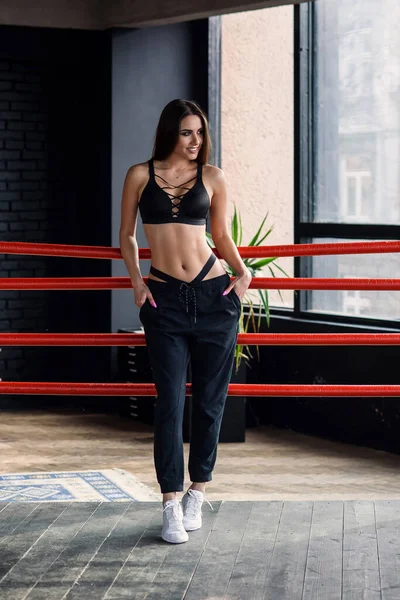 Sexy Fitness-Girl in Sportkleidung steht an Seilen des Boxrings gelehnt. — Stockfoto