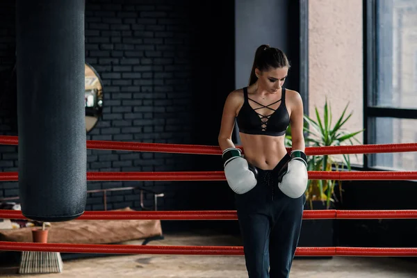 Menina caucasiana esportes atraentes apoiou-se nas cordas no ringue de boxe, ter um descanso após o treino intensivo no moderno ginásio loft . — Fotografia de Stock