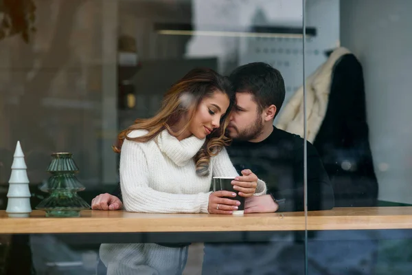 Cute girl with her boyfriend sitting inside a cafe and drinking hot fragrant coffee while outside is cold weather. Love and romance concept. — Stock Photo, Image