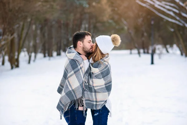 아름다운 한 쌍의 남녀가 서로 껴안고 침대보로 뒤덮여 있다. 잘 생긴 남자가 겨울 공원에서 예쁜 여자 친구에게 키스한다. — 스톡 사진