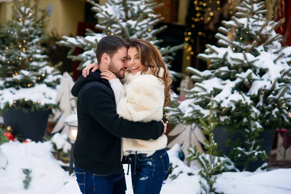 Ευτυχισμένο ζευγάρι με ζεστά ρούχα αγκαλιάζονται στο φόντο του χριστουγεννιάτικου δέντρου με φώτα. Χειμερινές διακοπές, Χριστούγεννα και Πρωτοχρονιά έννοια. — Φωτογραφία Αρχείου