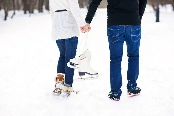 Закрыть любящую пару, гуляющую на свидании в зимнем парке. Молодой человек и его девушка держат друг друга за руки и держат коньки . — стоковое фото
