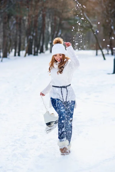 Krásná mladá žena nosila v bílém svetru a klobouk s bruslemi na rukou baví v zimě snowy park. — Stock fotografie