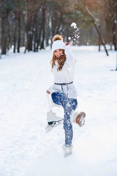 Krásná mladá žena nosila v bílém svetru a klobouk s bruslemi na rukou baví v zimě snowy park. — Stock fotografie