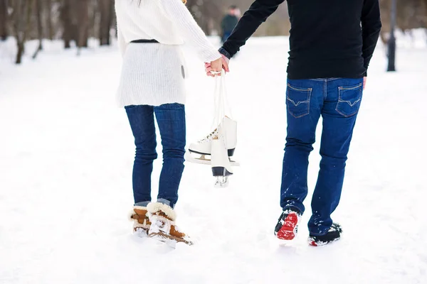 De cerca pareja amorosa caminando en una cita en un parque de invierno. Joven y su novia se agarran a las manos y sostienen patines de hielo . — Foto de Stock