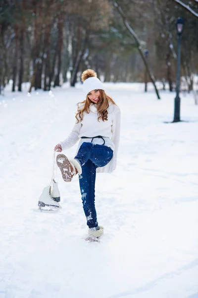 Krásná mladá žena nosila v bílém svetru a klobouk s bruslemi na rukou baví v zimě snowy park. — Stock fotografie