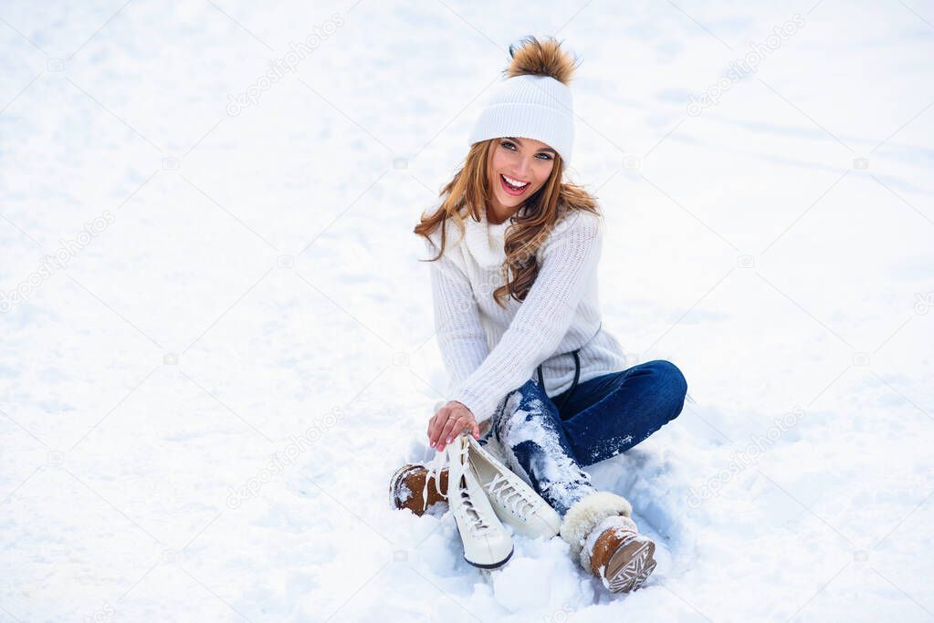 Young woman sits on the frosty snow in winter park. Winter holidays concept.