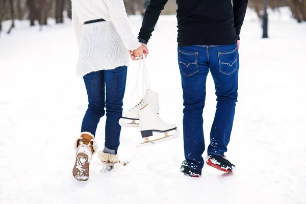 Gros plan couple amoureux marchant sur un rendez-vous dans un parc d'hiver. Jeune homme et sa petite amie se tient les mains et tenant des patins à glace . — Photo