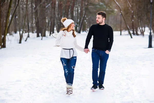 可爱的一对情侣在冬天的公园里约会。 在女孩们的背上挂着一双冰鞋. — 图库照片
