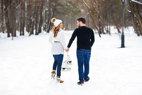 Gros plan couple amoureux marchant sur un rendez-vous dans un parc d'hiver. Jeune homme et sa petite amie se tient les mains et tenant des patins à glace . — Photo