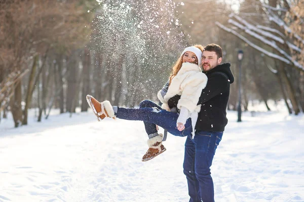 Jeune couple élégant amoureux amusez-vous en marchant sur le parc d'hiver enneigé. Beau jeune homme tient sa belle fille sur les mains . — Photo