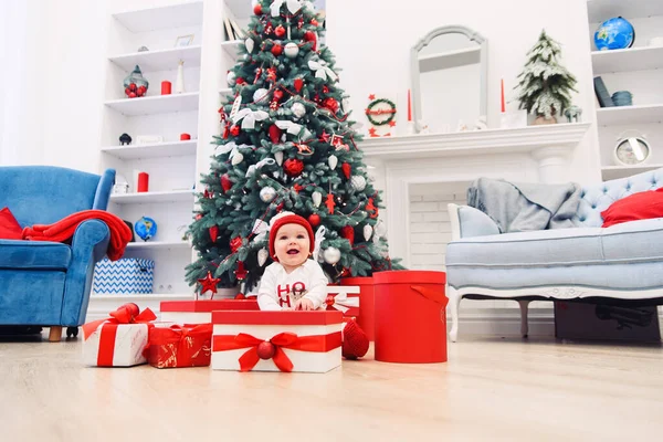 Charmante petite fille tient boîte cadeau de Noël blanc avec ruban rouge. Bébé mignon drôle porté en vêtements de fête dans la chambre décorée de Noël. Concept de Noël et vacances du Nouvel An . — Photo